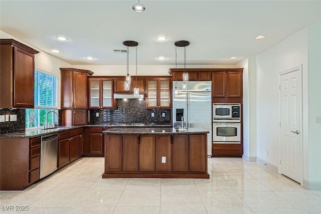 kitchen featuring built in appliances, a sink, a center island, dark stone countertops, and glass insert cabinets