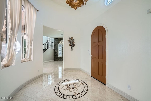 foyer with arched walkways, a chandelier, stairs, and baseboards