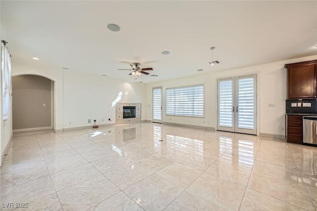 unfurnished living room featuring arched walkways, ceiling fan, visible vents, baseboards, and a glass covered fireplace