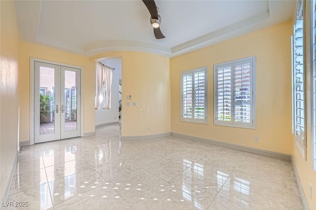 empty room with arched walkways, a raised ceiling, marble finish floor, and french doors