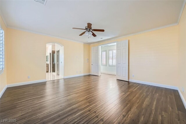 spare room with dark wood-style floors, arched walkways, ornamental molding, and baseboards