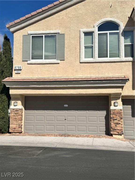 view of side of property with a garage, stone siding, and stucco siding