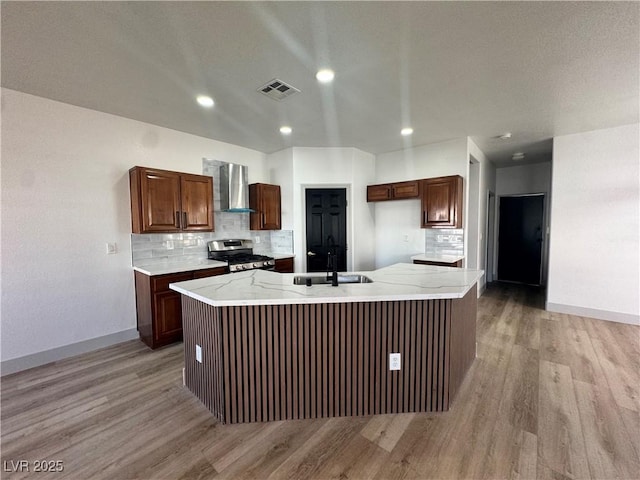 kitchen with visible vents, a sink, gas range, light wood-type flooring, and wall chimney exhaust hood