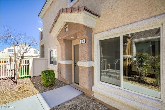 view of exterior entry featuring stucco siding and fence