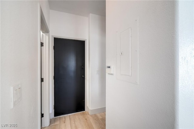 corridor with electric panel, light wood-type flooring, and baseboards