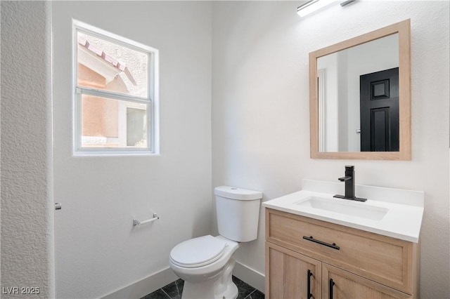 half bathroom with baseboards, vanity, and toilet