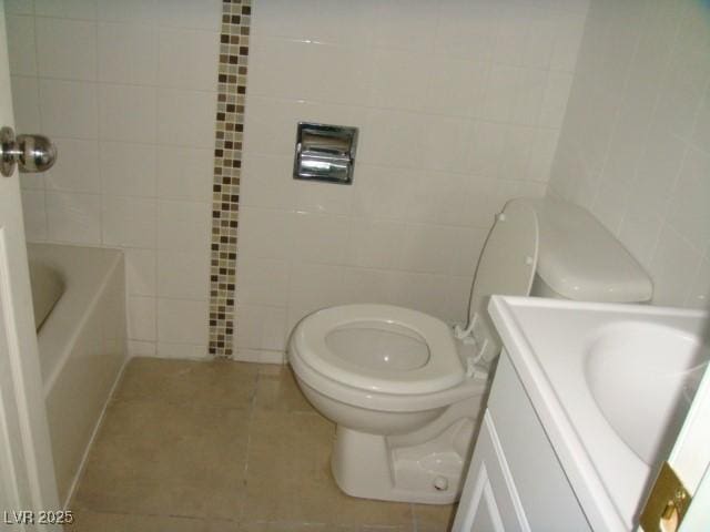 bathroom featuring tile walls, toilet, a bathing tub, vanity, and tile patterned floors