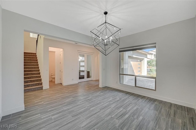 unfurnished dining area featuring a chandelier, stairway, wood finished floors, and baseboards