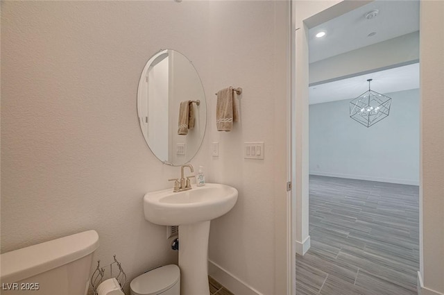 bathroom featuring an inviting chandelier, baseboards, toilet, and wood finished floors