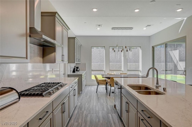 kitchen with wall chimney exhaust hood, light stone countertops, stainless steel appliances, gray cabinetry, and a sink