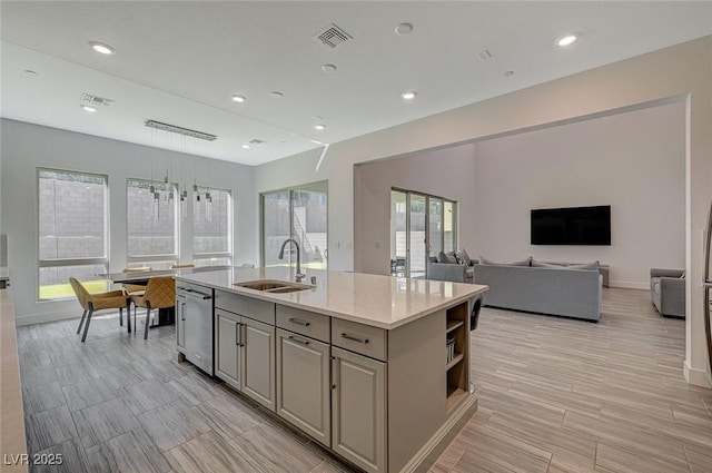 kitchen featuring open shelves, visible vents, gray cabinetry, a sink, and an island with sink