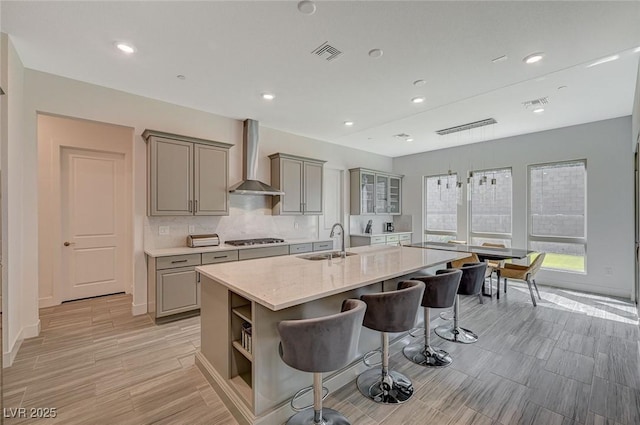 kitchen featuring visible vents, wall chimney exhaust hood, gray cabinetry, stainless steel gas cooktop, and a sink