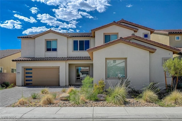 mediterranean / spanish home with decorative driveway, a tiled roof, an attached garage, and stucco siding