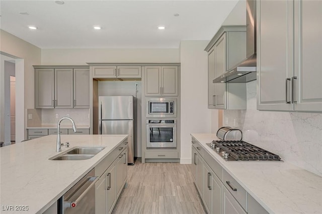 kitchen with stainless steel appliances, a sink, wall chimney range hood, and light stone counters