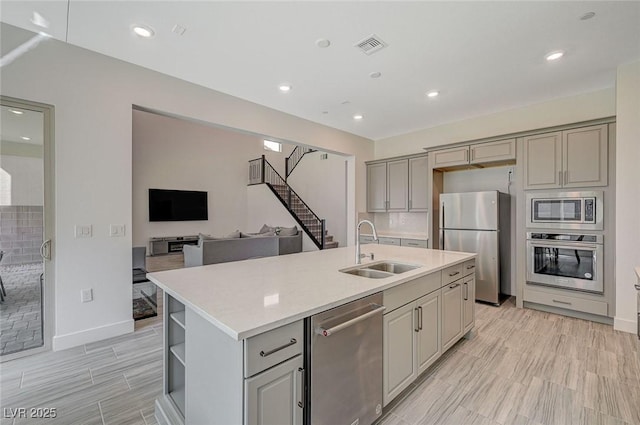 kitchen featuring a sink, open floor plan, appliances with stainless steel finishes, gray cabinets, and an island with sink