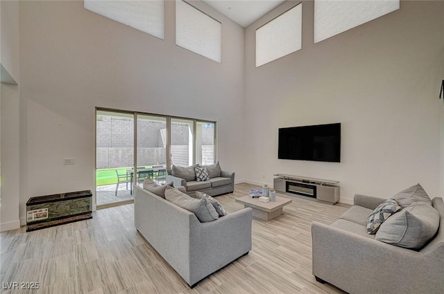 living room with a high ceiling, baseboards, and light wood finished floors