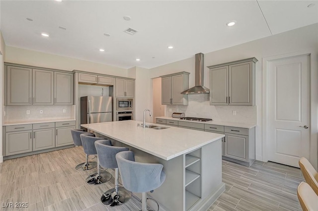 kitchen featuring stainless steel appliances, gray cabinets, a sink, and wall chimney exhaust hood