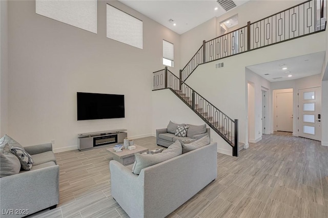 living room with light wood-style flooring, stairway, visible vents, and baseboards