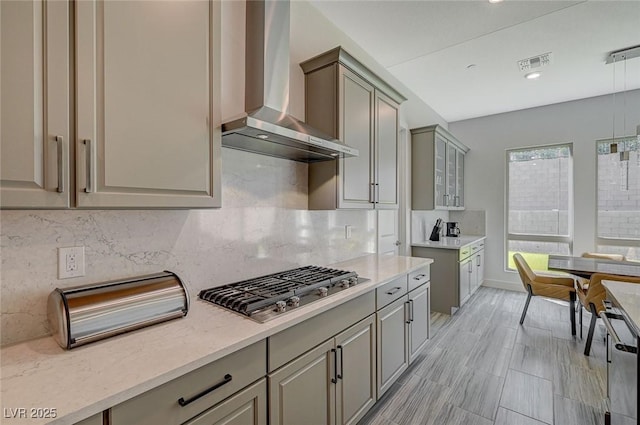 kitchen featuring gray cabinets, visible vents, stainless steel gas stovetop, decorative backsplash, and wall chimney range hood