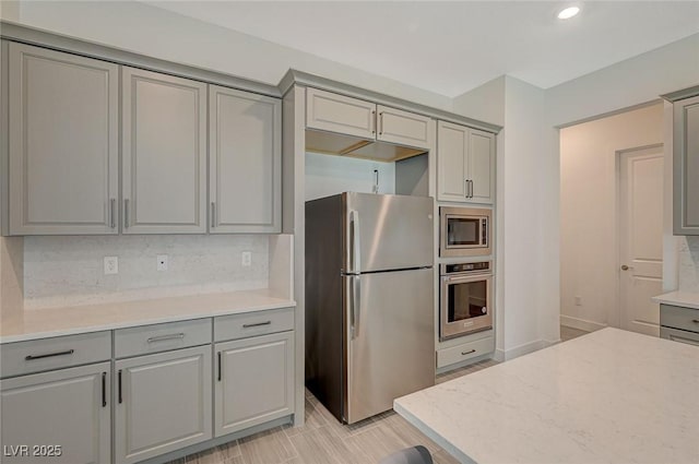 kitchen with appliances with stainless steel finishes, recessed lighting, backsplash, and gray cabinetry