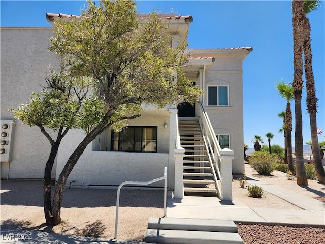 view of front of house featuring a tiled roof, stairway, and stucco siding