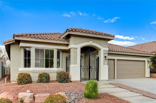 mediterranean / spanish-style house featuring concrete driveway, a tile roof, an attached garage, a gate, and stucco siding