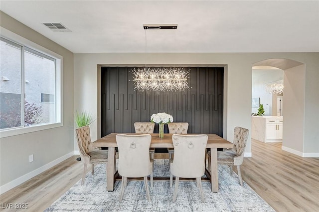 dining room with arched walkways, visible vents, baseboards, light wood-style floors, and an inviting chandelier