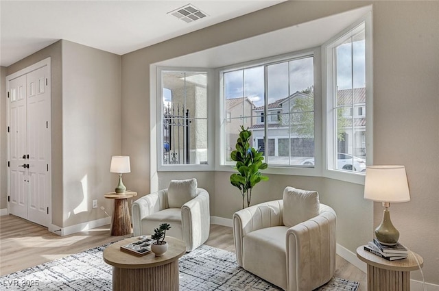 living area with light wood-type flooring, visible vents, and baseboards