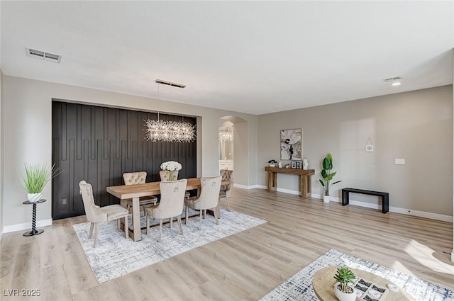 dining space with visible vents, arched walkways, a chandelier, and light wood-style flooring