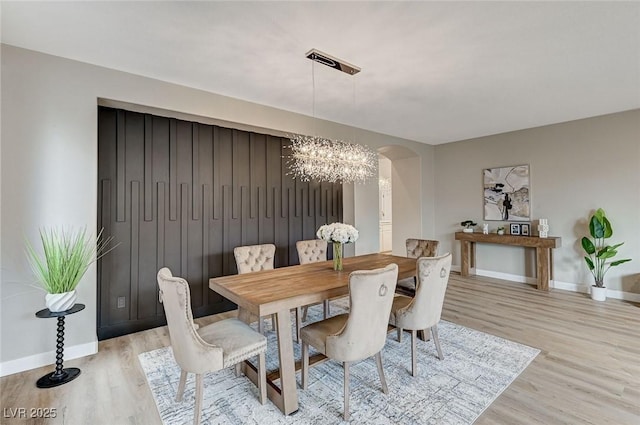 dining space with an inviting chandelier, light wood-style flooring, arched walkways, and baseboards