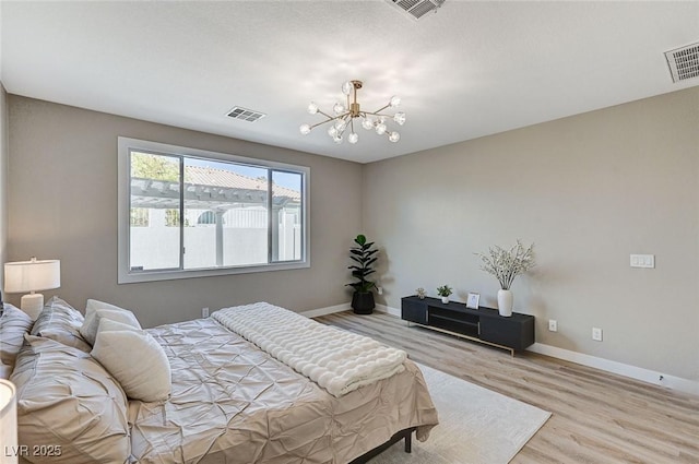 bedroom featuring baseboards, wood finished floors, visible vents, and an inviting chandelier