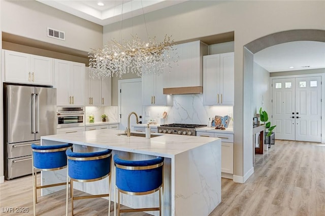 kitchen featuring a center island with sink, visible vents, arched walkways, appliances with stainless steel finishes, and a sink