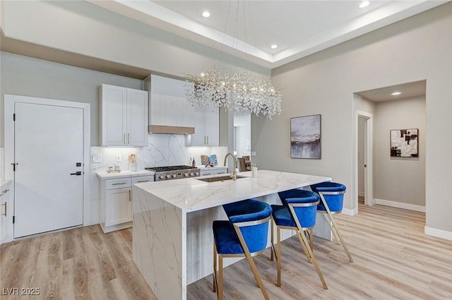 kitchen with a sink, light stone countertops, light wood finished floors, a kitchen bar, and a center island with sink