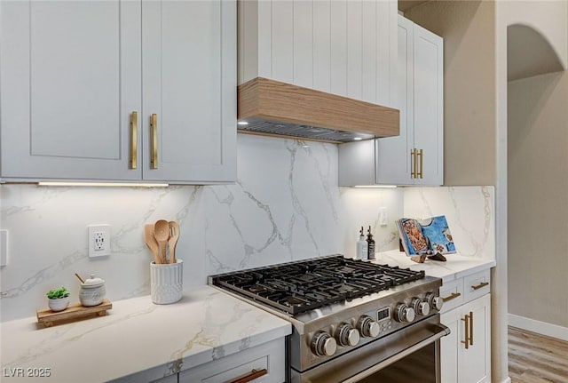 kitchen featuring backsplash, custom exhaust hood, high end range, and light stone countertops