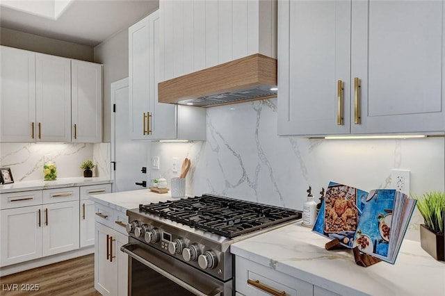 kitchen with custom exhaust hood, light stone countertops, stainless steel range, and white cabinets