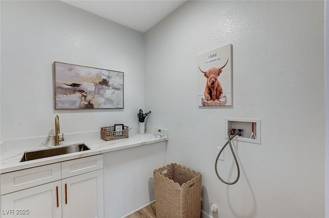 clothes washing area featuring hookup for a washing machine, cabinet space, a sink, and wood finished floors