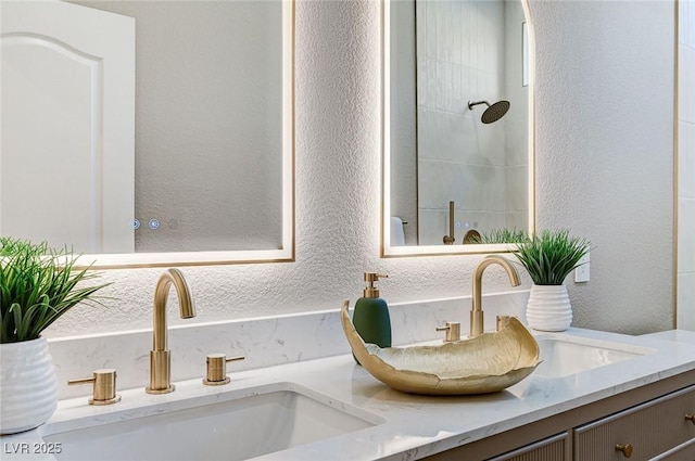 details featuring a textured wall, a sink, a tile shower, and double vanity