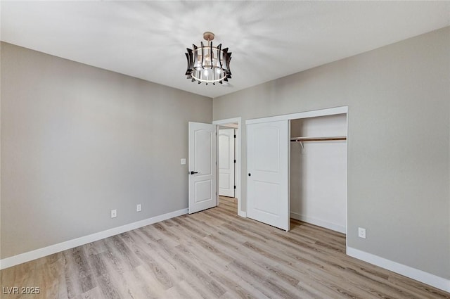 unfurnished bedroom with a closet, a notable chandelier, baseboards, and wood finished floors