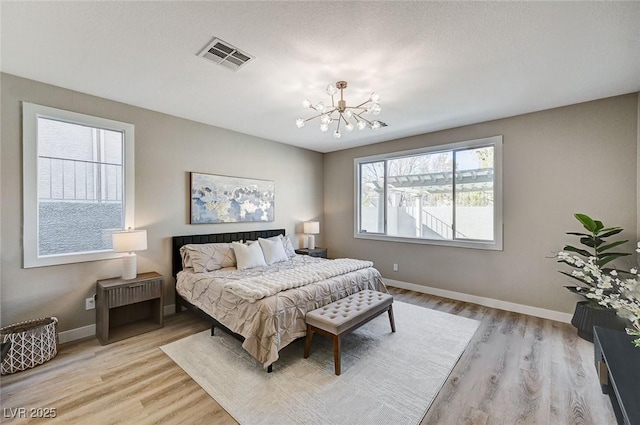 bedroom with a notable chandelier, light wood-style flooring, visible vents, and baseboards