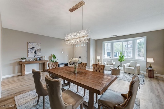 dining room featuring a chandelier, light wood-style flooring, visible vents, and baseboards