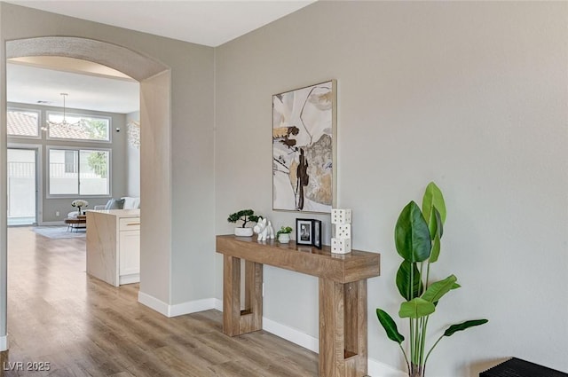 corridor featuring arched walkways, light wood-style flooring, and baseboards