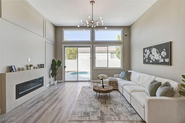 living area with a chandelier, a glass covered fireplace, baseboards, and wood finished floors