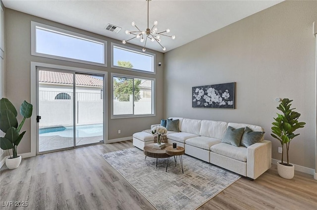 living area featuring a chandelier, wood finished floors, visible vents, and baseboards