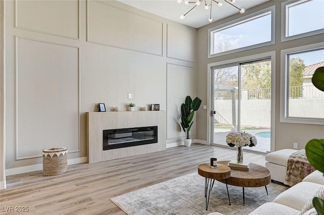 living room featuring a glass covered fireplace, a notable chandelier, a towering ceiling, and wood finished floors