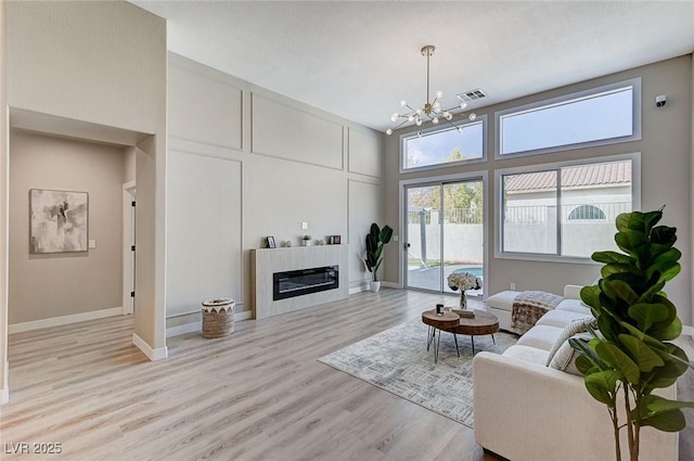 living room featuring wood finished floors, a towering ceiling, visible vents, a glass covered fireplace, and an inviting chandelier