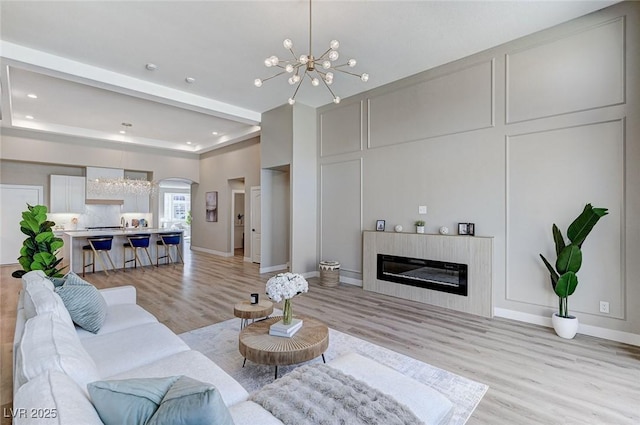 living area with a decorative wall, a glass covered fireplace, light wood-style flooring, and a notable chandelier