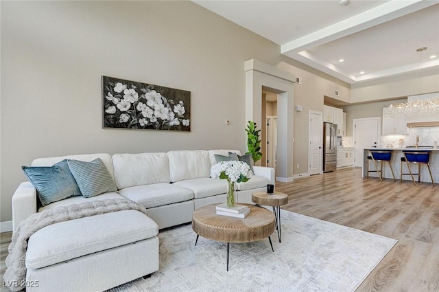 living room with light wood finished floors, baseboards, a high ceiling, a tray ceiling, and recessed lighting