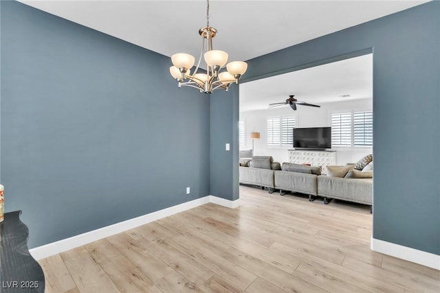 unfurnished living room with ceiling fan with notable chandelier, baseboards, and light wood finished floors