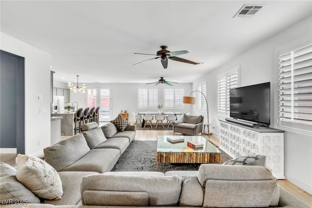 living room with visible vents, ceiling fan with notable chandelier, baseboards, and light wood finished floors