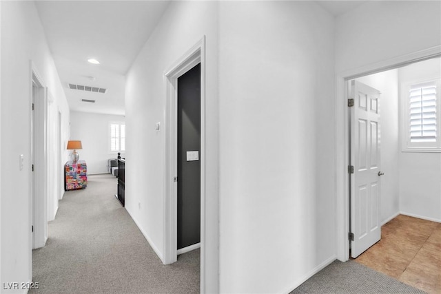 corridor featuring baseboards, visible vents, and light carpet